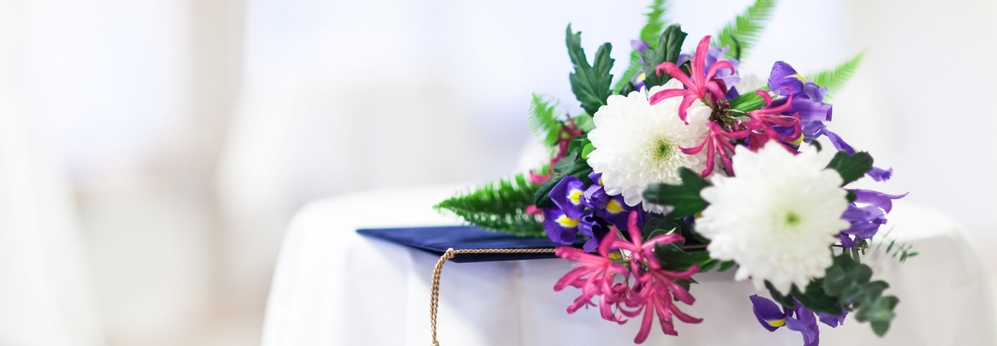 Vaalea tausta, valkoisella pöydällä kukkakimppu ja todistuskansio.