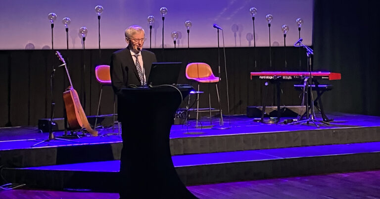 Elias-palkinnon voittanut Kari Haukipuro pitämässä puhetta Duodecimin iltajuhlassa. Taustalla bändin varusteet ja koristeellisia valaisimia. Sininen juhlavalaistus.