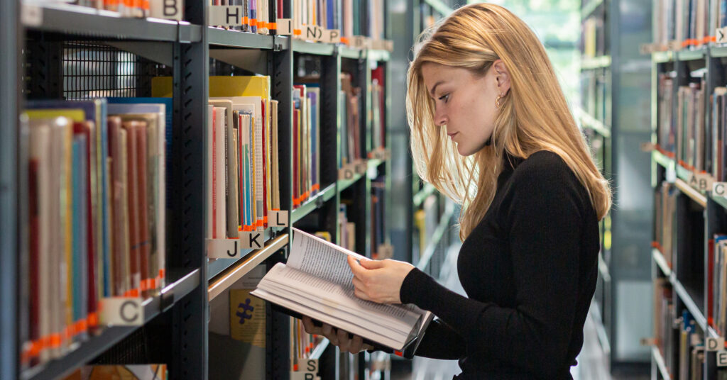 Henkilö selaa kirjoja kirjastossa.